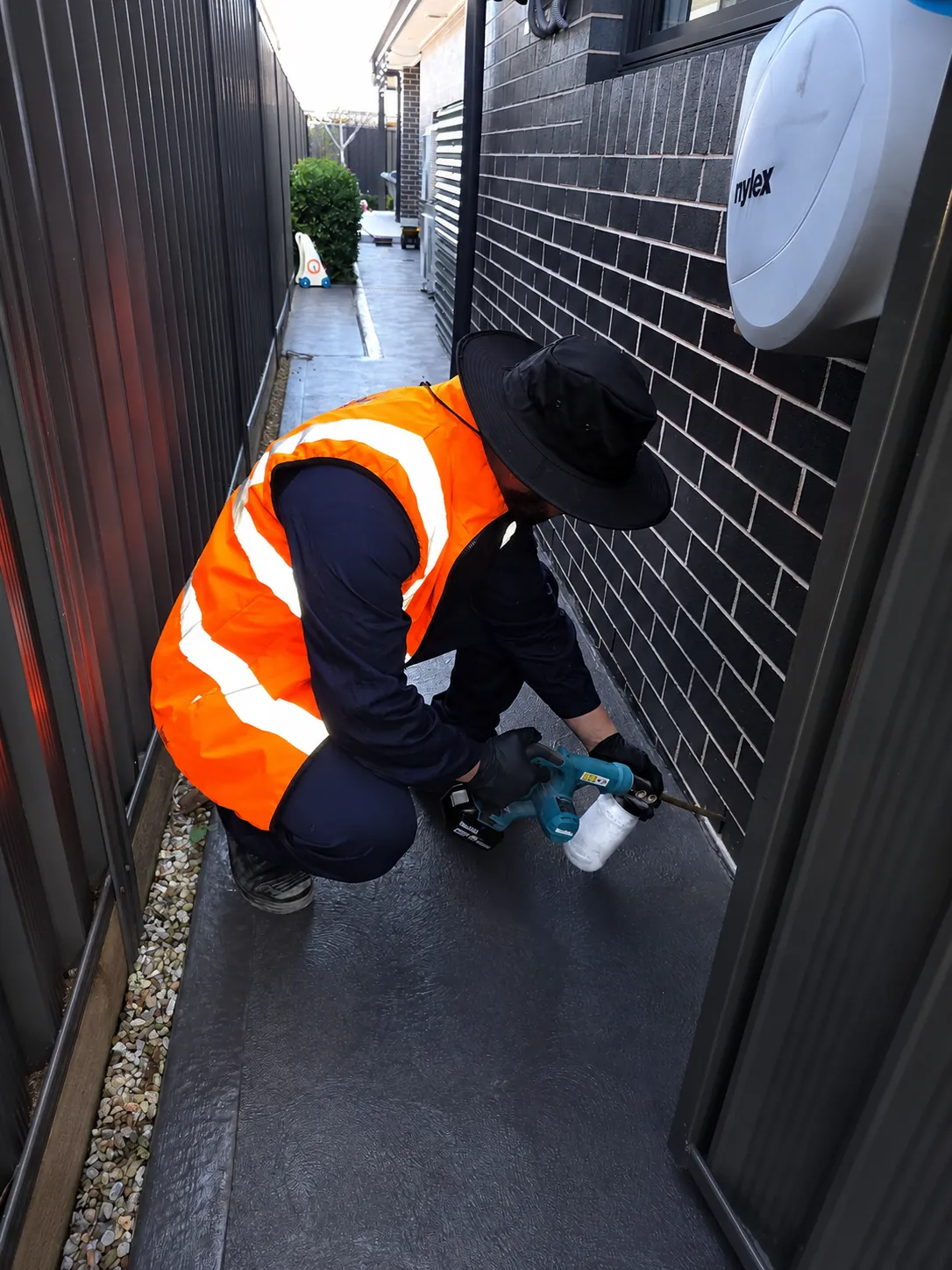 Aries Pest Solutions technician applying insecticide dust into the weep holes along a brick wall
